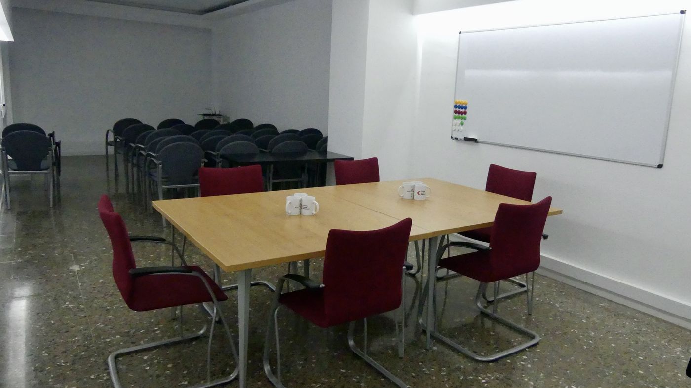 Sala de reuniones grande de 40 m² con mesa de reuniones, pizarra blanca y filas de sillas con pala al fondo